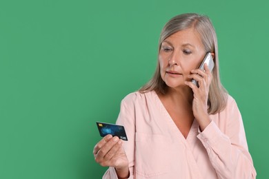 Worried woman with credit card talking on smartphone against green background, space for text. Be careful - fraud