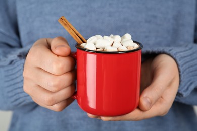 Photo of Woman holding cup of delicious hot chocolate with marshmallows and cinnamon stick, closeup