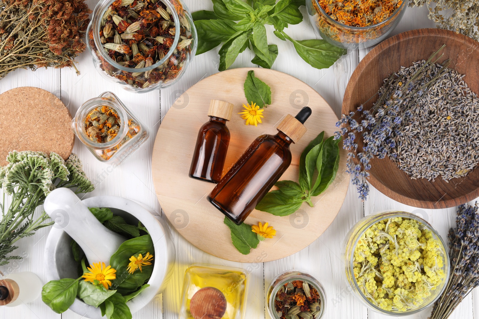 Photo of Bottles of essential oils surrounded by different herbs on white wooden table, flat lay