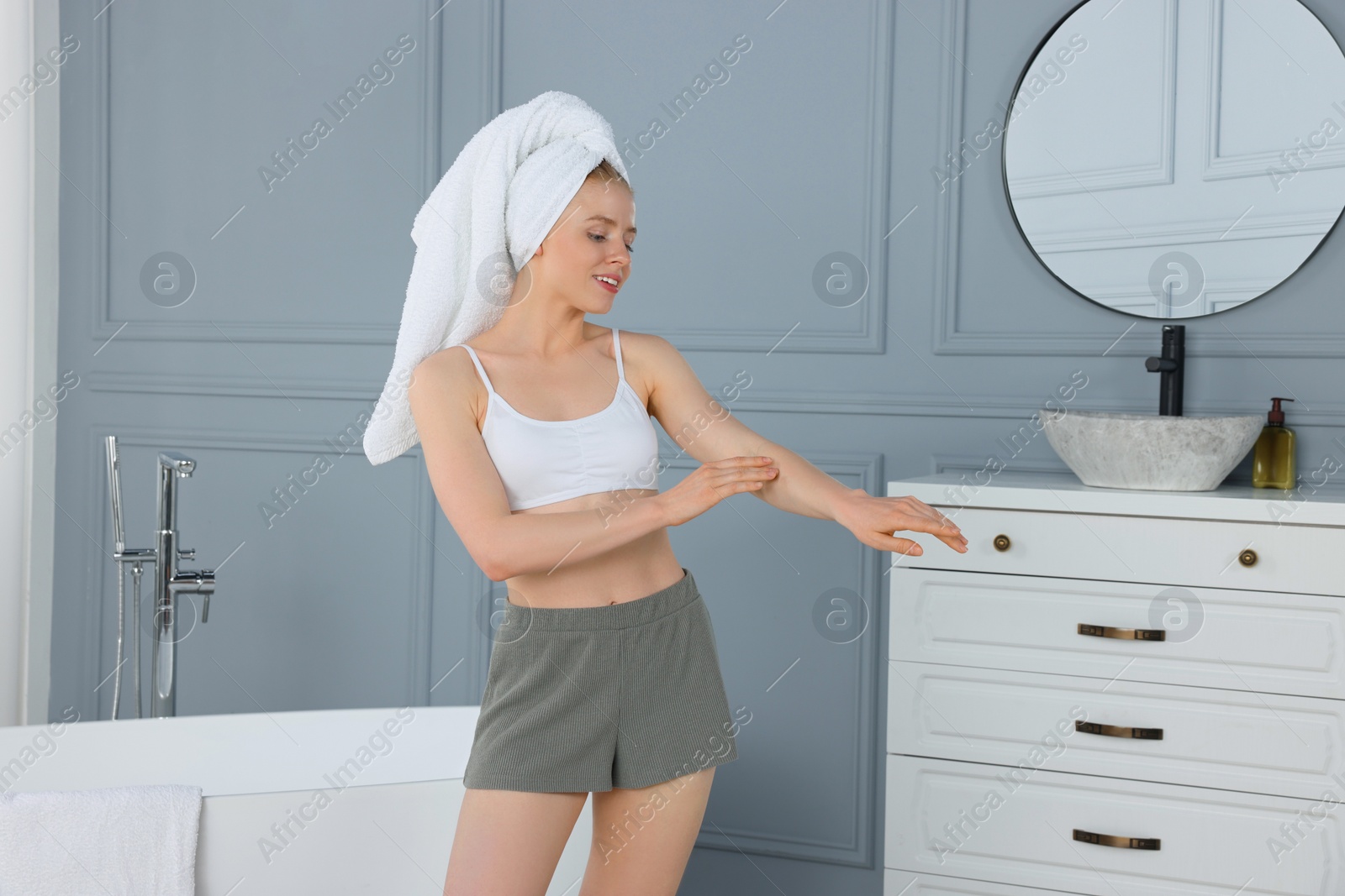 Photo of Beautiful young woman applying body cream onto arm in bathroom