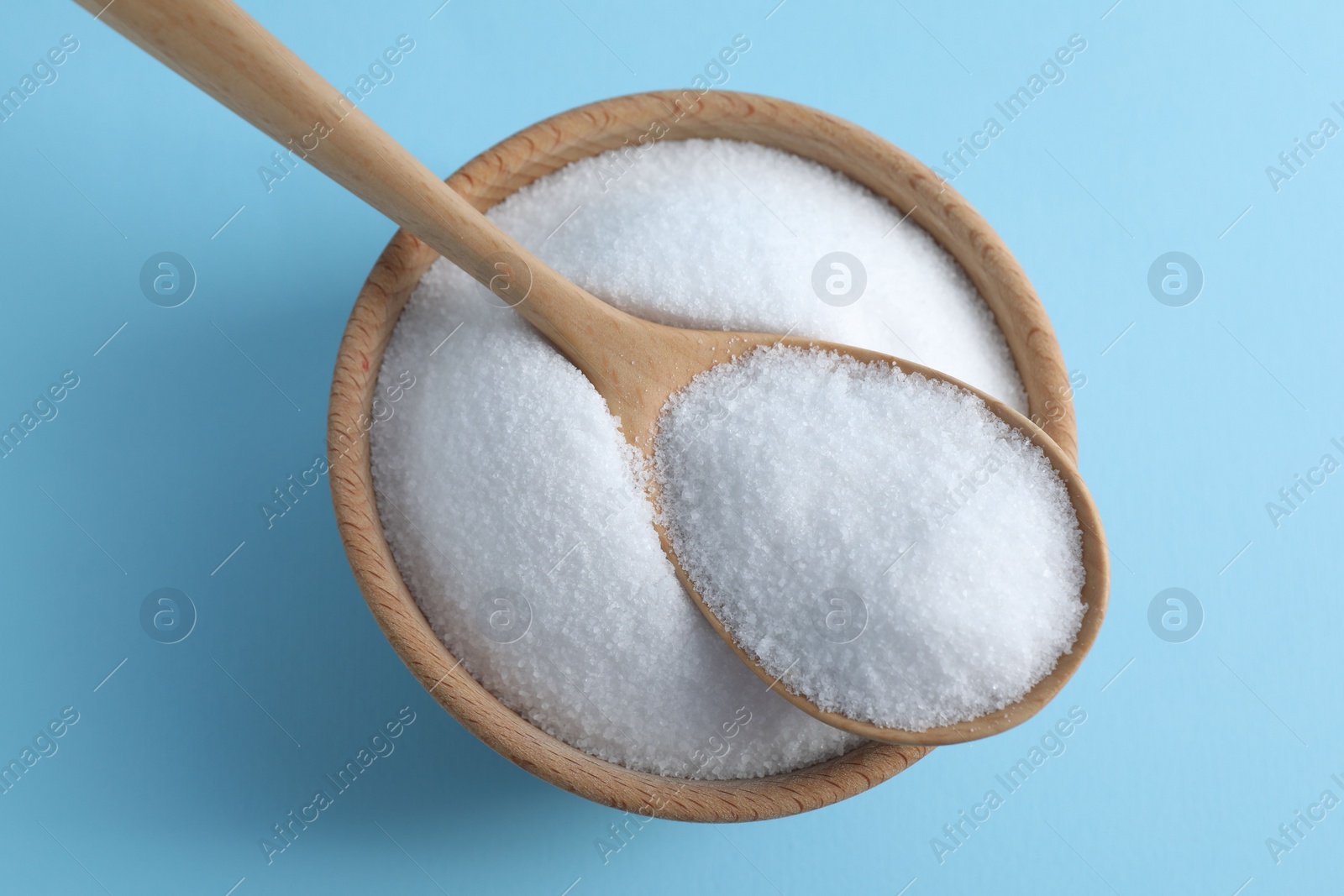 Photo of Organic white salt in bowl and spoon on light blue background, top view