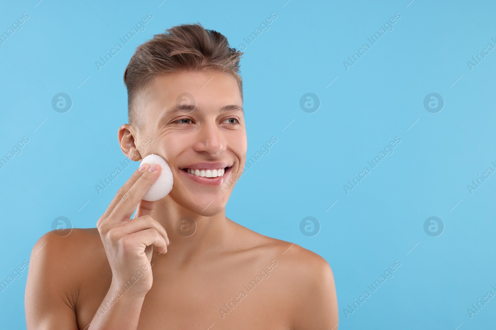 Photo of Happy young man washing his face with sponge on light blue background. Space for text