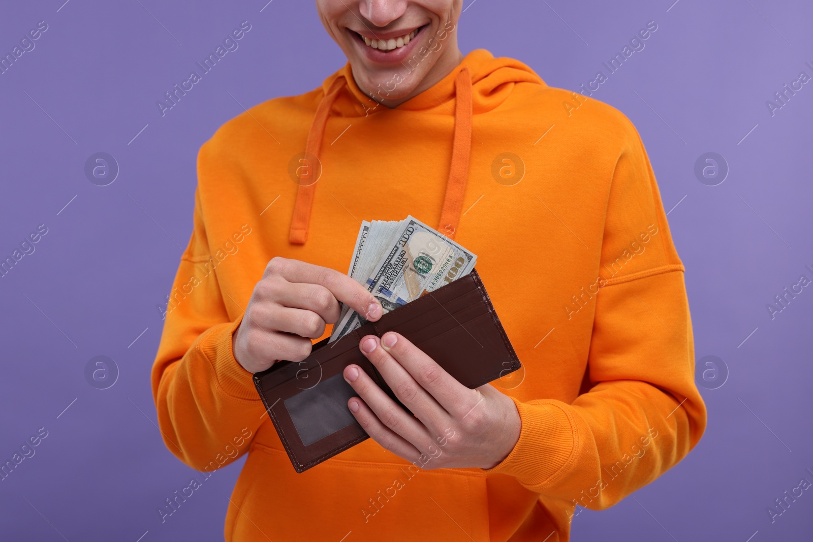 Photo of Happy man putting money into wallet on purple background, closeup