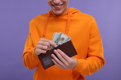 Happy man putting money into wallet on purple background, closeup