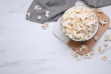 Bowl of tasty popcorn on white marble table, flat lay. Space for text