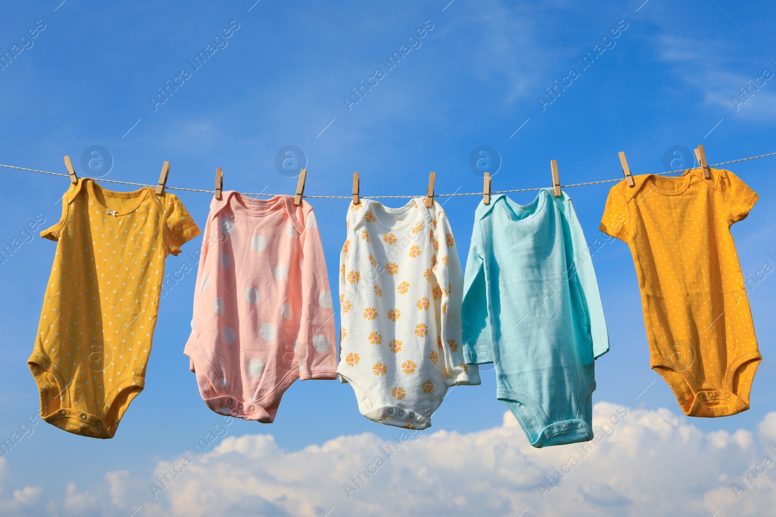 Photo of Clean baby onesies hanging on washing line against sky. Drying clothes