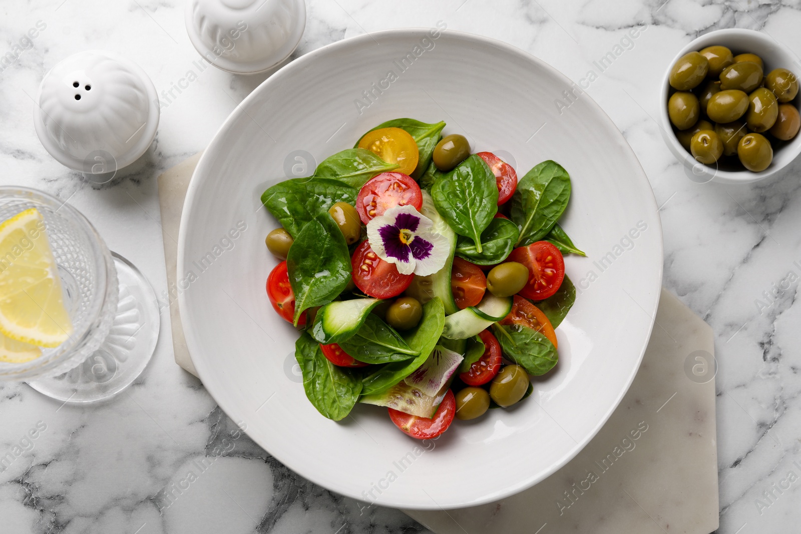 Photo of Delicious salad with vegetables and olives served on white marble table, flat lay