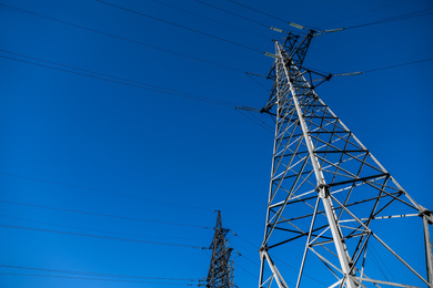 Modern high voltage tower against blue sky, low angle view