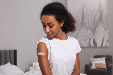 Photo of Young woman with adhesive bandage on her arm after vaccination indoors