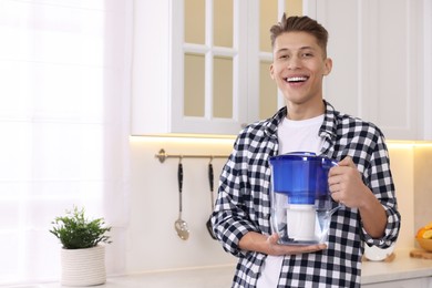 Photo of Happy man with water filter jug in kitchen. Space for text