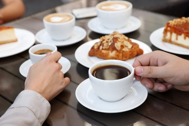 Photo of Friends drinking coffee at wooden table in outdoor cafe, closeup