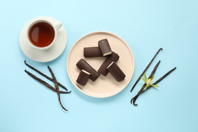 Photo of Glazed curd cheese bars, vanilla pods and tea on light blue background, flat lay