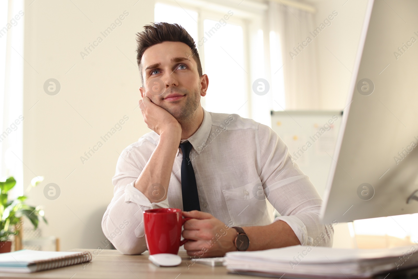 Photo of Young businessman with cup of drink relaxing at table in office during break