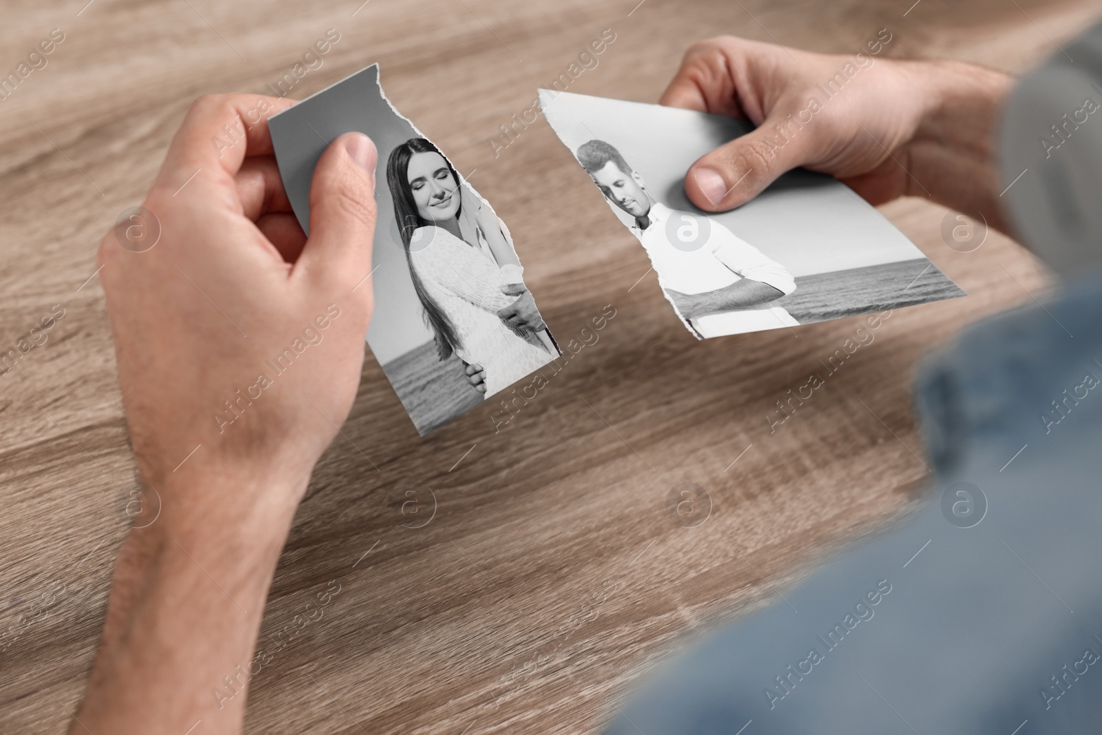 Image of Divorce and breakup. Man holding parts of ripped black and white photo at table, closeup