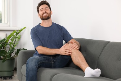 Photo of Man suffering from leg pain on sofa at home