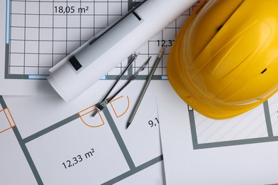 Photo of Rolled construction drawing, safety hat, pair of compasses and pencil on house plan, flat lay