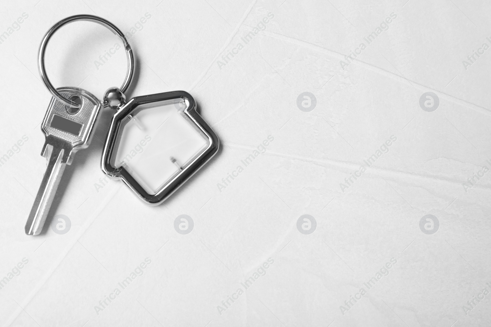 Photo of Key with trinket in shape of house on light grey stone background, top view and space for text. Real estate agent services