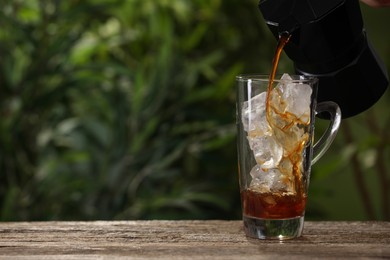 Photo of Pouring coffee over ice in glass cup at wooden table outdoors. Space for text