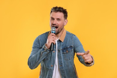 Handsome man with microphone singing on yellow background