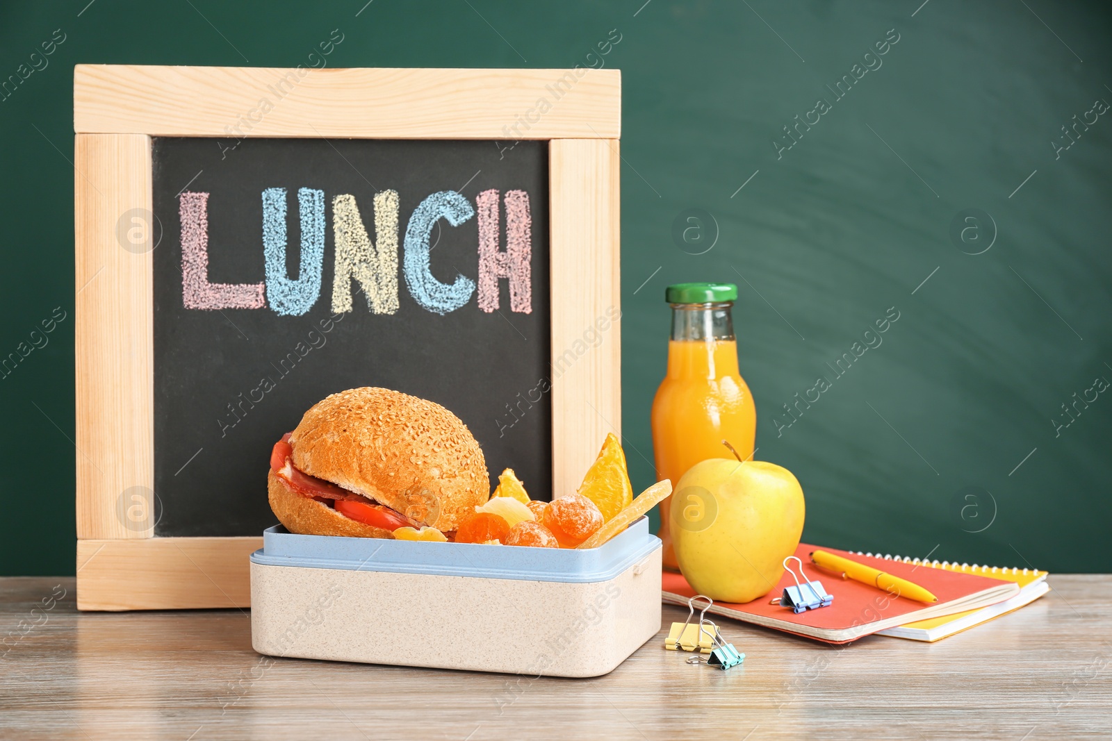 Photo of Lunch box with appetizing food, small blackboard and notebooks on table