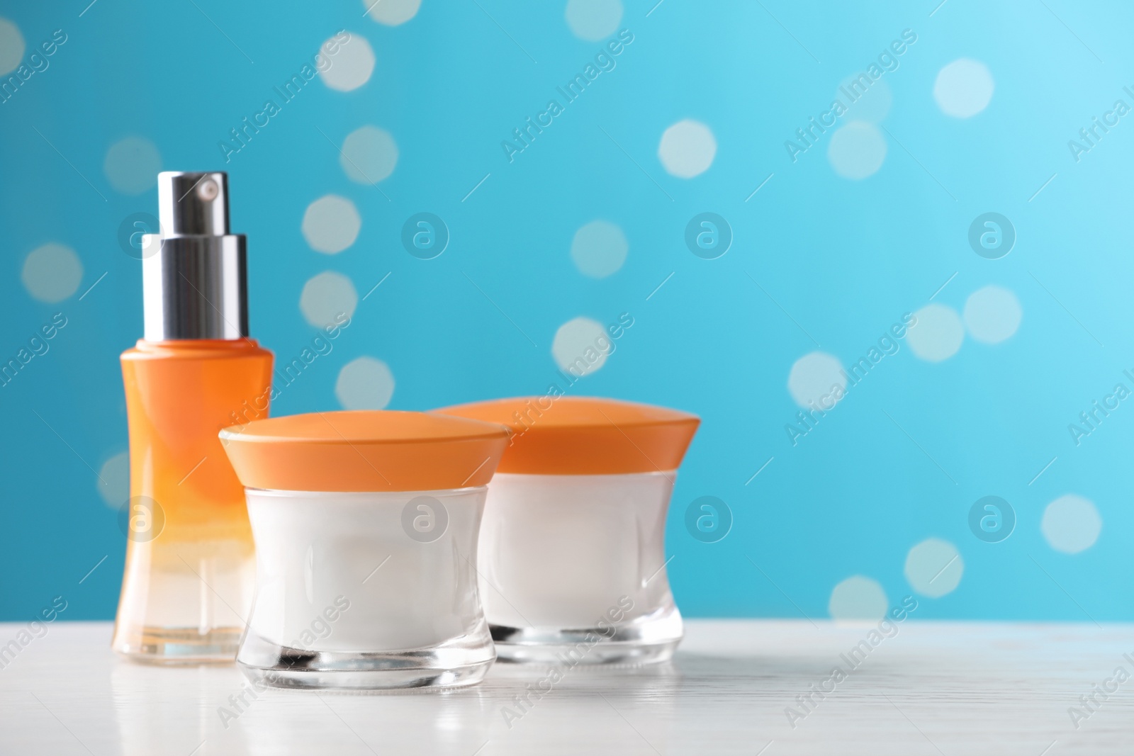 Photo of Skin care products on white wooden table against blurred lights, space for text