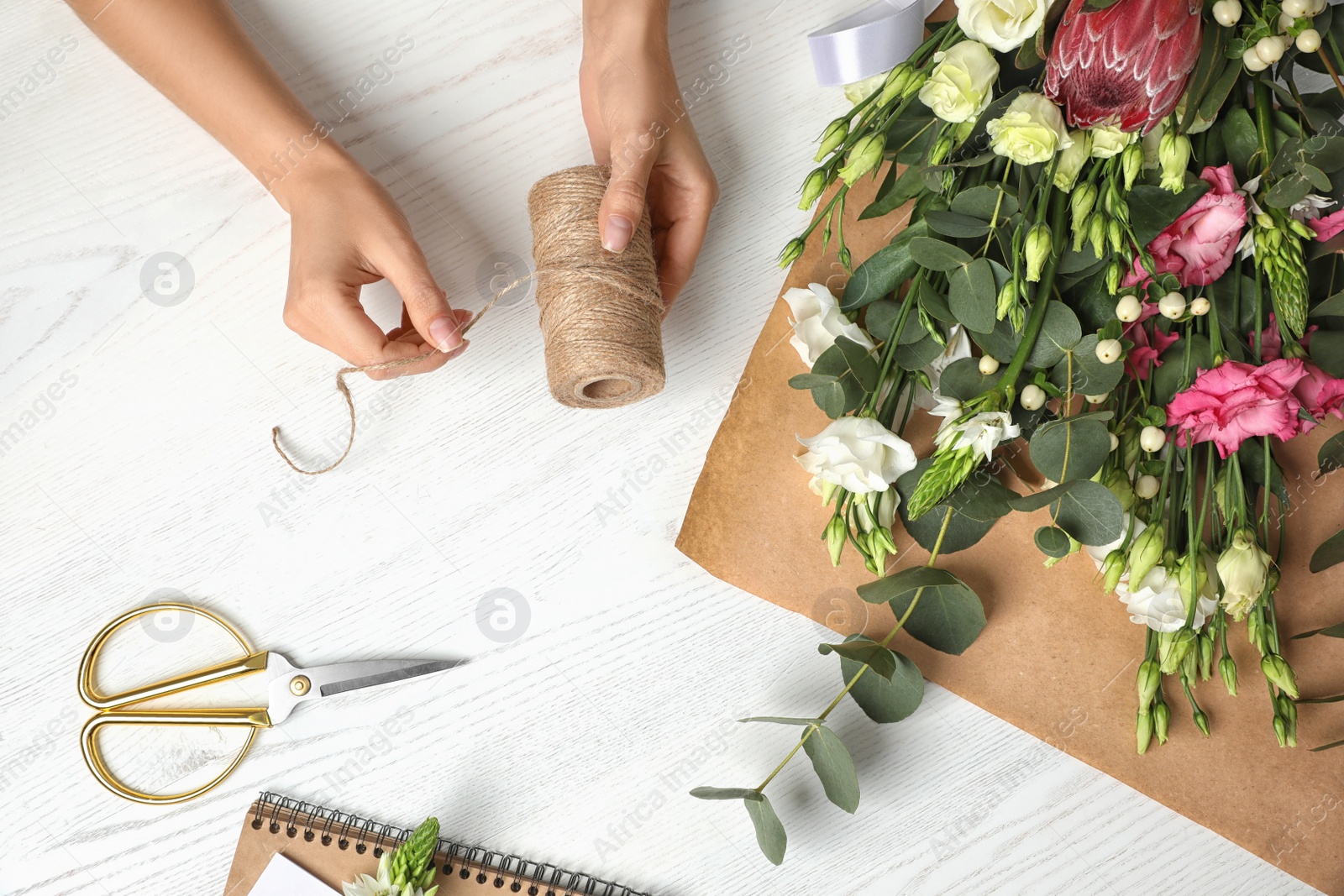 Photo of Florist making beautiful bouquet at white wooden table, top view