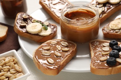 Photo of Toasts with different nut butters, banana slices, blueberries and nuts on white table, closeup