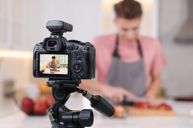 Photo of Food blogger cooking while recording video in kitchen, focus on camera