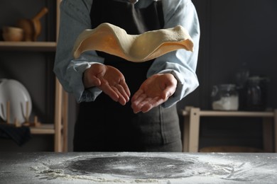 Photo of Woman tossing pizza dough at table in kitchen, closeup