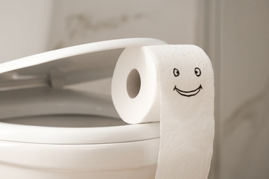 Roll of paper with funny face on toilet bowl in bathroom, closeup