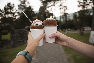 Couple holding delicious desserts with whipped cream on city street, closeup