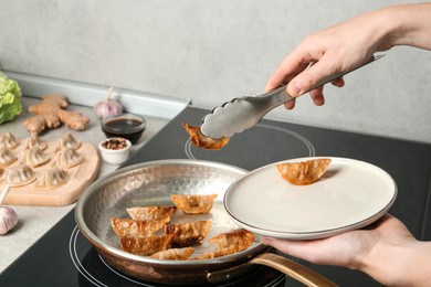 Photo of Woman serving freshly cooked delicious gyoza on plate in kitchen, closeup