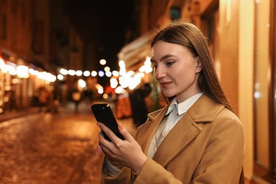 Photo of Beautiful woman using smartphone on night city street. Space for text