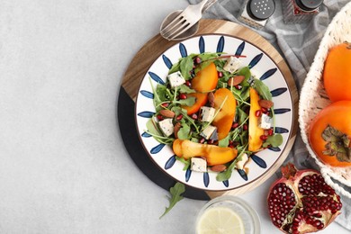 Photo of Tasty salad with persimmon, blue cheese, pomegranate and almonds served on white table, flat lay. Space for text