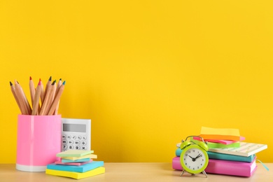 Different school stationery and alarm clock on table against yellow background, space for text. Back to school