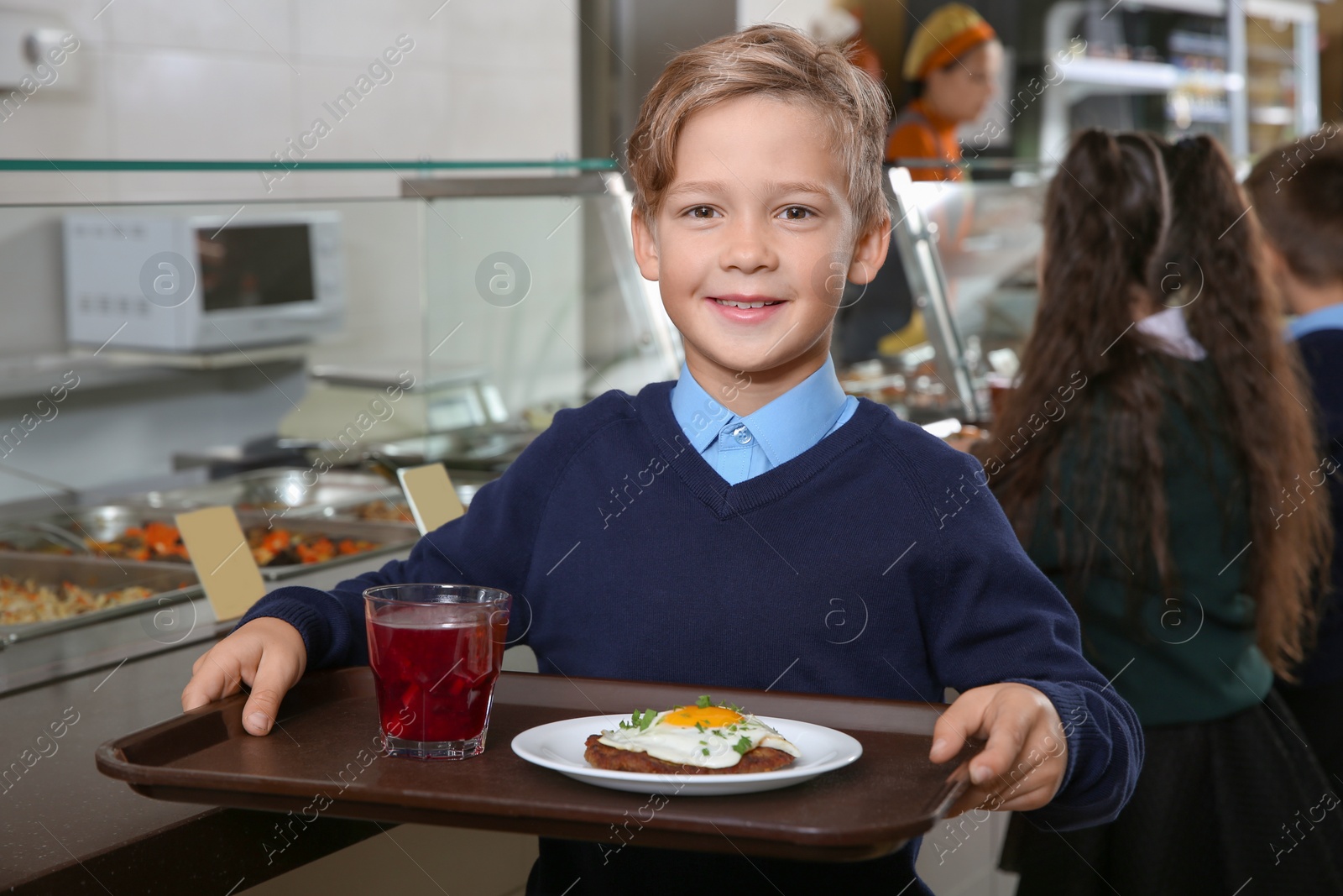 Photo of Cute boy holding tray with healthy food in school canteen