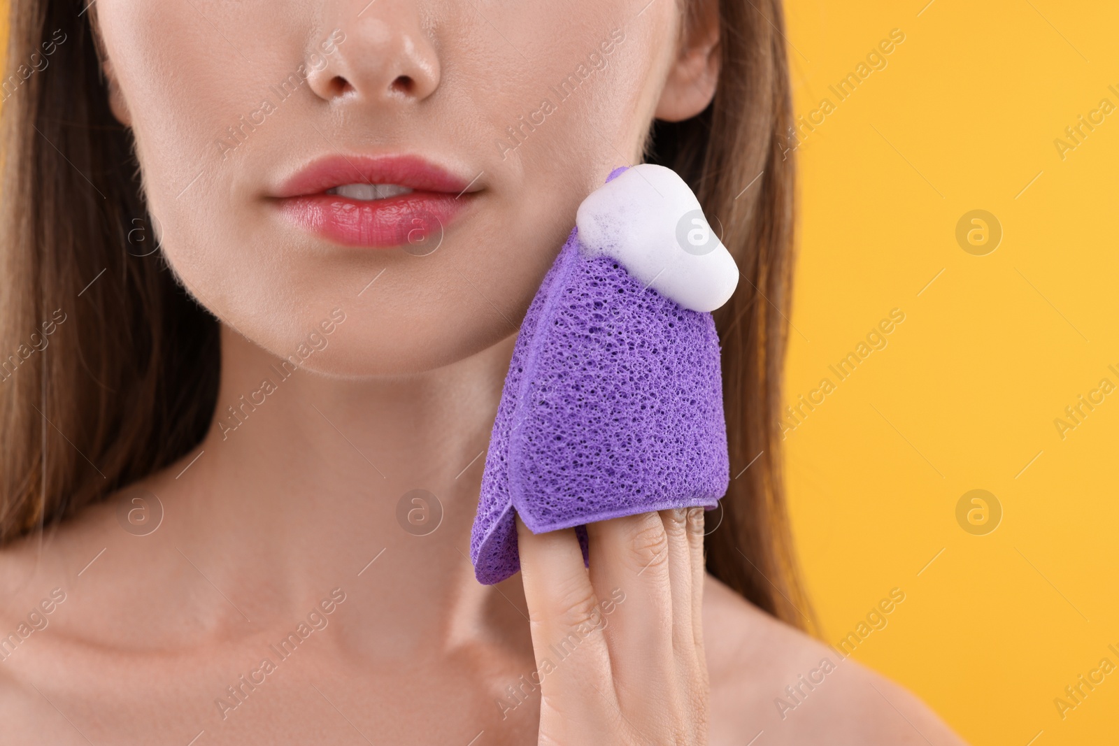 Photo of Happy young woman washing her face with sponge on orange background, closeup