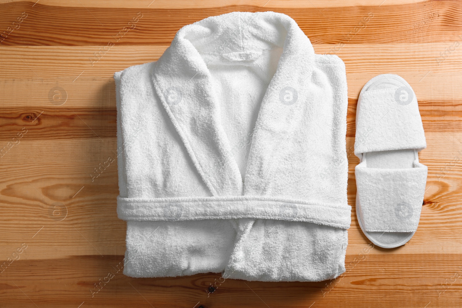 Photo of Clean folded bathrobe and slippers on wooden background, flat lay