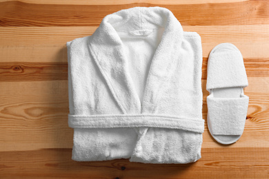 Photo of Clean folded bathrobe and slippers on wooden background, flat lay