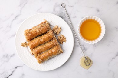 Photo of Eastern sweets. Pieces of tasty baklava and honey on white marble table, top view