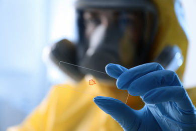 Photo of Scientist in chemical protective suit with microscope slide on light background, focus on hand. Virus research