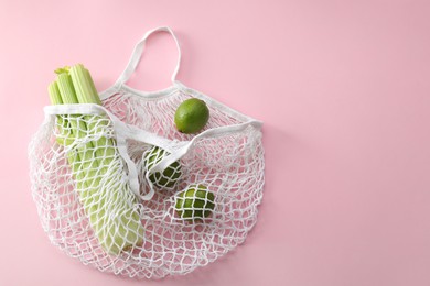 String bag with celery and limes on pink background, top view. Space for text