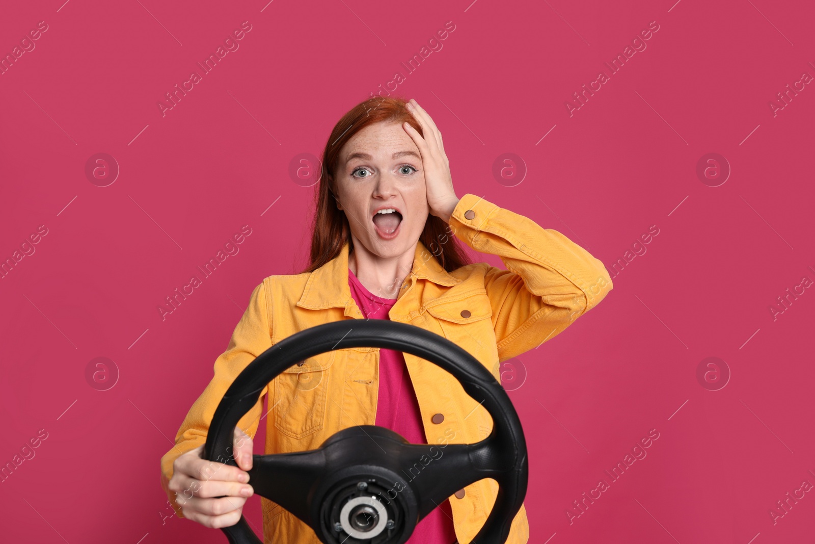 Photo of Emotional young woman with steering wheel on crimson background