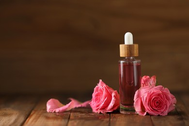 Photo of Bottle of essential rose oil and flowers on wooden table, space for text