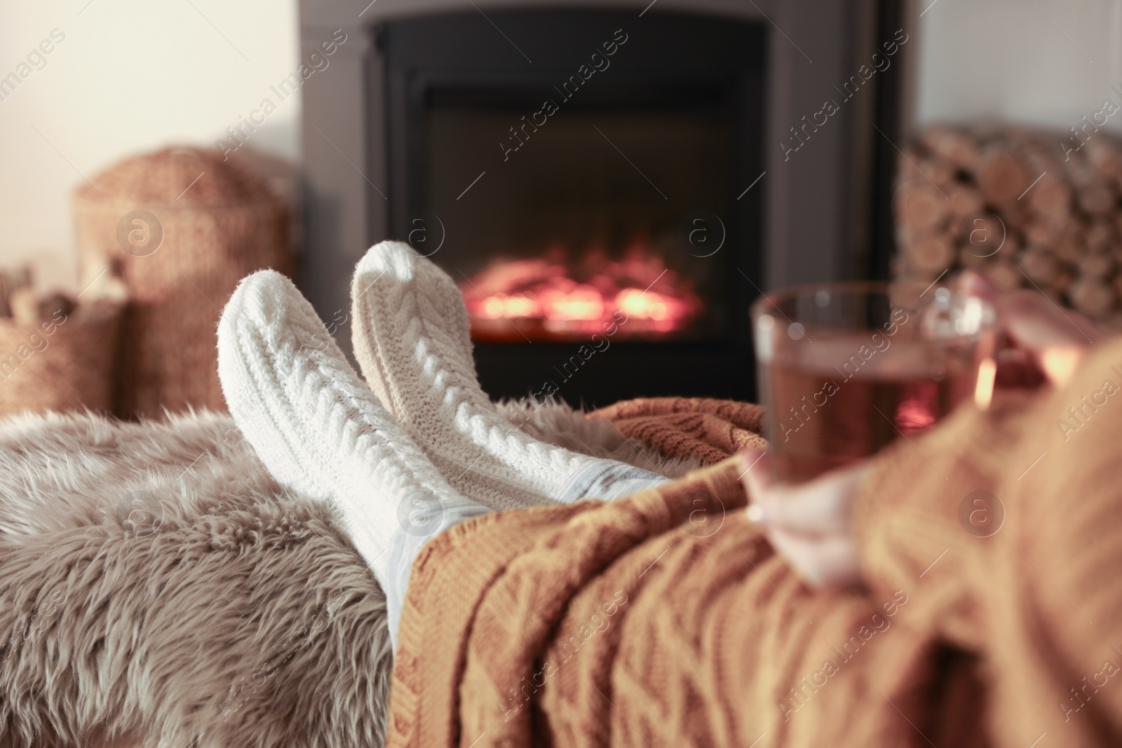 Photo of Woman with cup of tea resting near fireplace at home, closeup