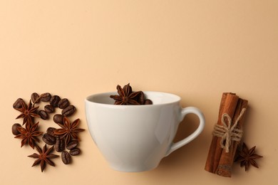 Photo of Cup with coffee beans, anise stars and cinnamon sticks on beige background, flat lay. Space for text
