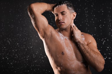 Photo of Man washing hair while taking shower on black background