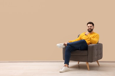 Photo of Handsome man sitting in armchair near beige wall indoors, space for text