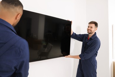 Photo of Male movers carrying plasma TV near white wall indoors