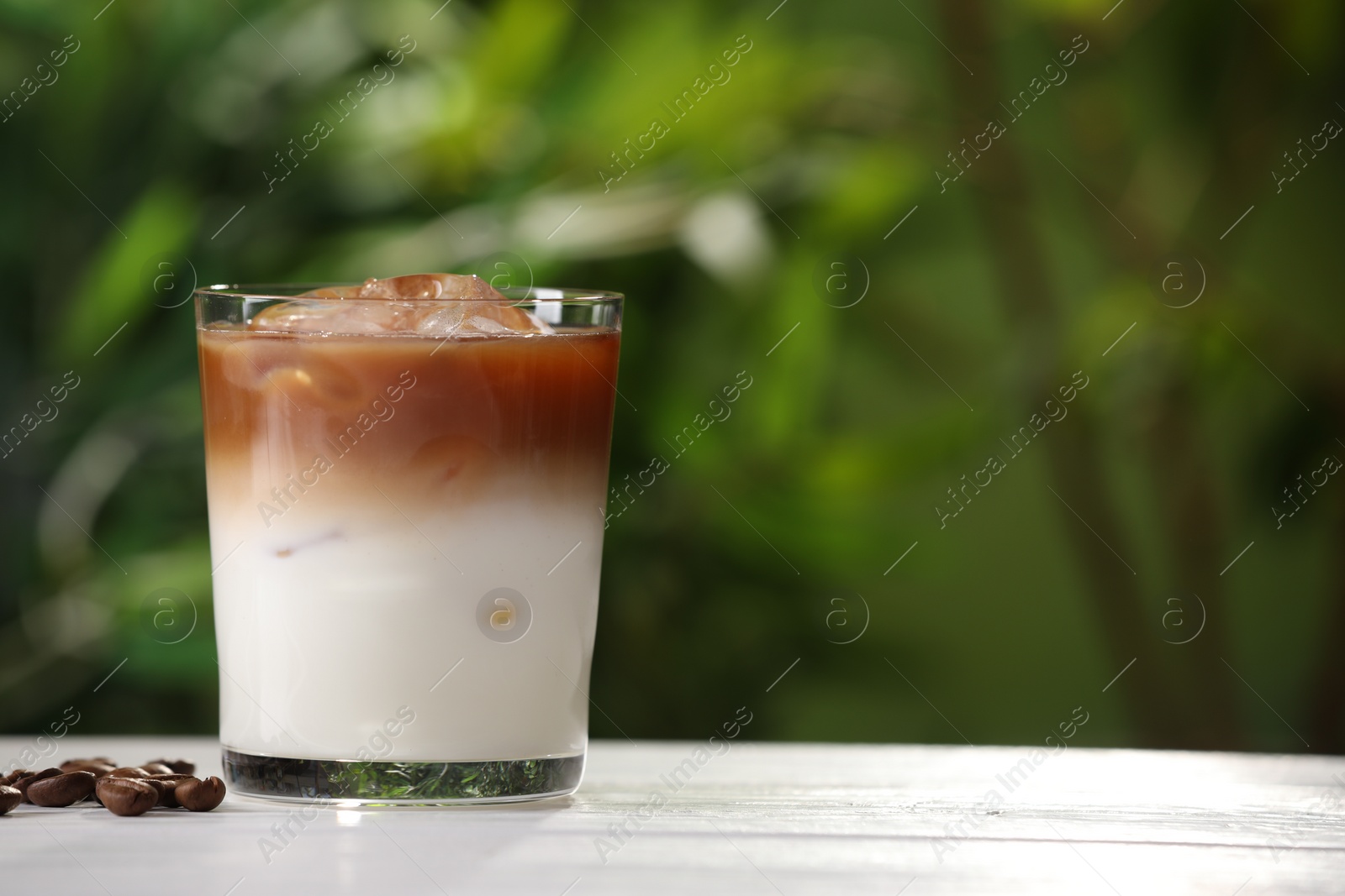 Photo of Glass of iced coffee and beans on white wooden table outdoors. Space for text